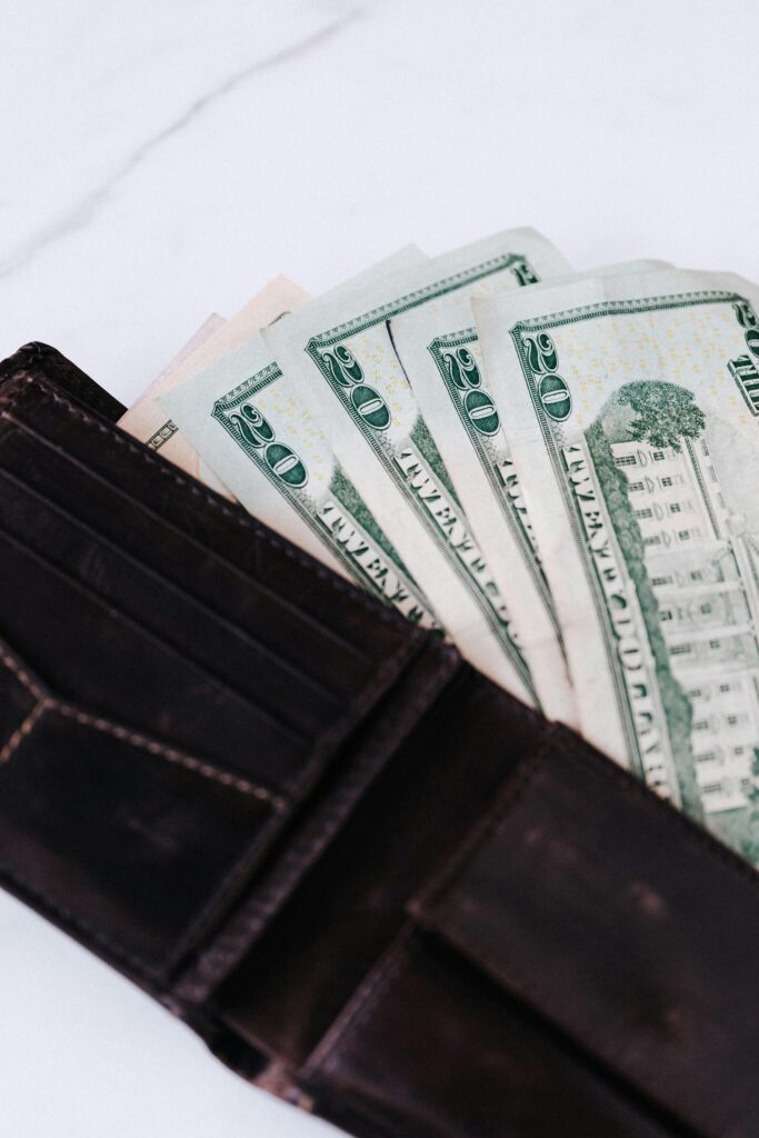 From above of black leather wallet with cash money of twenty dollars placed on white table